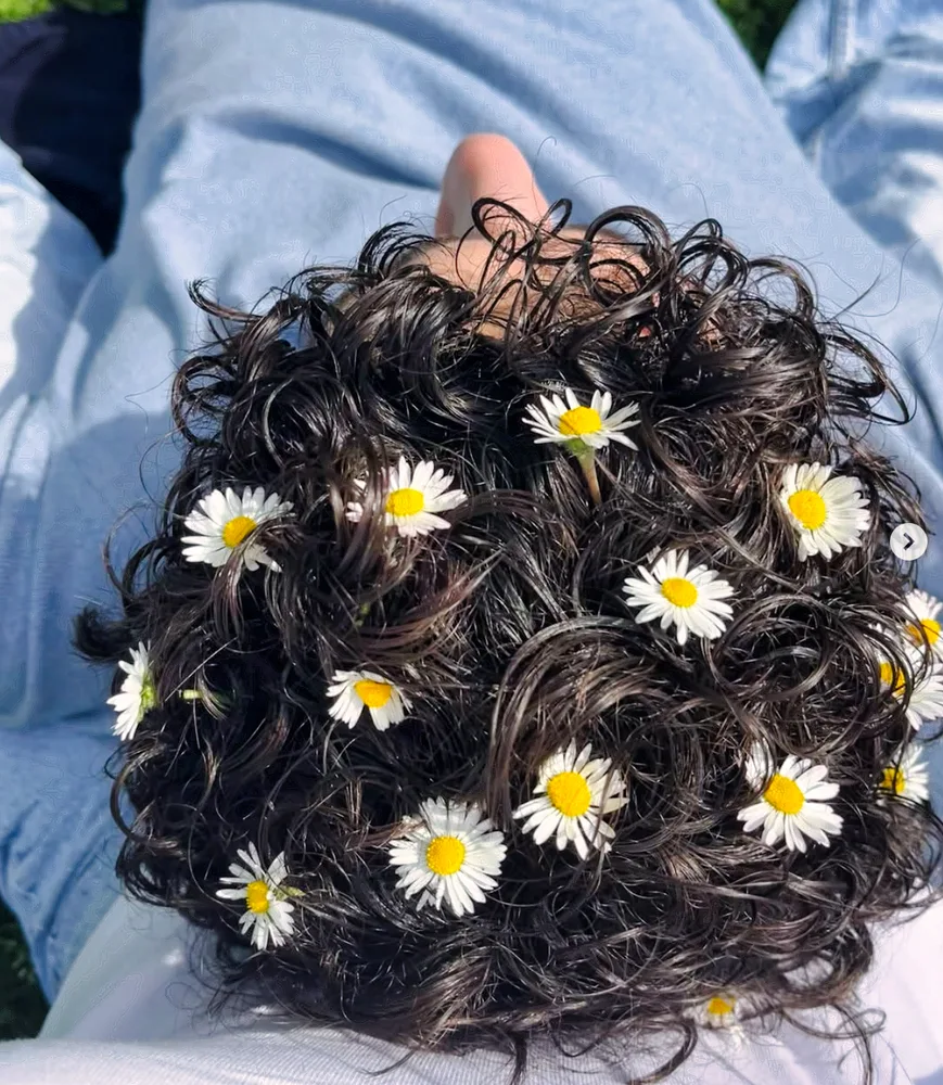 Lockiges Haar mit eingeflochtenen Gänseblümchen